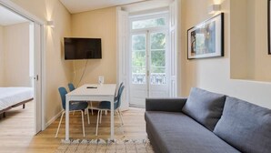 A modern room with a grey sofa, a dining table with chairs, a TV mounted on the wall, and a door leading to an outdoor balcony. - Setúbal Prime IV, Apartment (Setúbal)