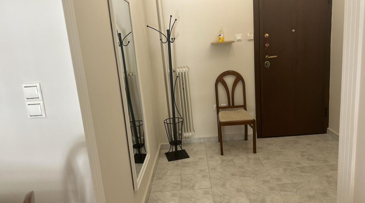 A hallway with a radiator, a coat rack, a chair, and a door.
