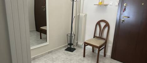 A small room with a wooden chair, a coat rack, a radiator, and a door with a handle.
