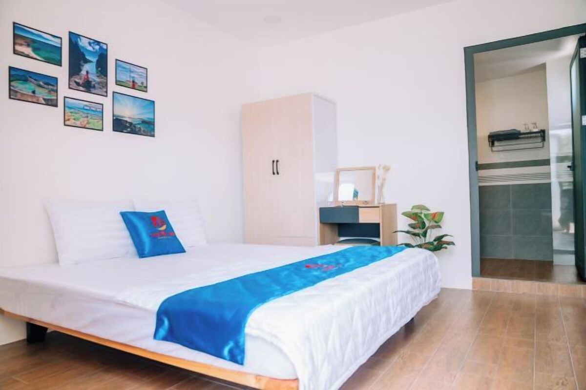 A hotel room with a bed, a wardrobe, a desk, and a bathroom visible through an open door.