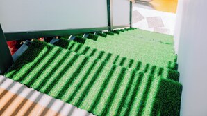 A staircase with green artificial grass leading to a balcony with a colorful sunset mural. - Thuyen Xua Homestay Phu Quy Island (Phu Quy)