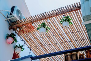 Een pergola van bamboe met hangende plantenbakken en een plafondventilator.