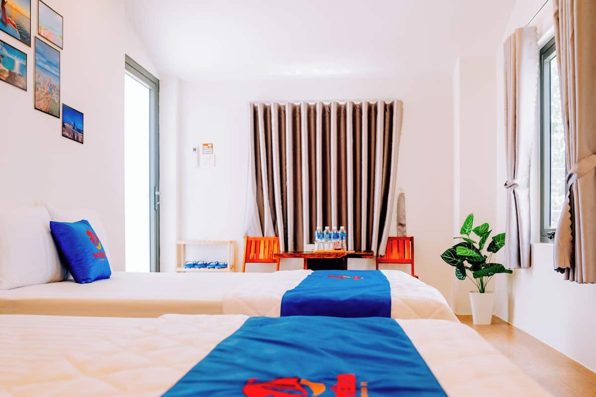 Habitación de hotel con dos camas, un escritorio con silla, una planta en maceta y una ventana con cortinas.
