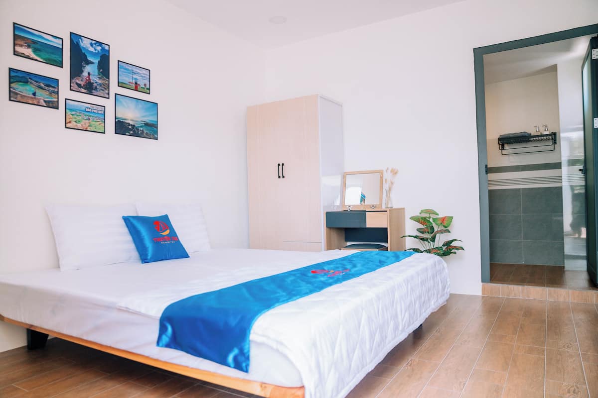 Habitación de hotel con cama, armario, escritorio, espejo y baño visible a través de una puerta abierta.