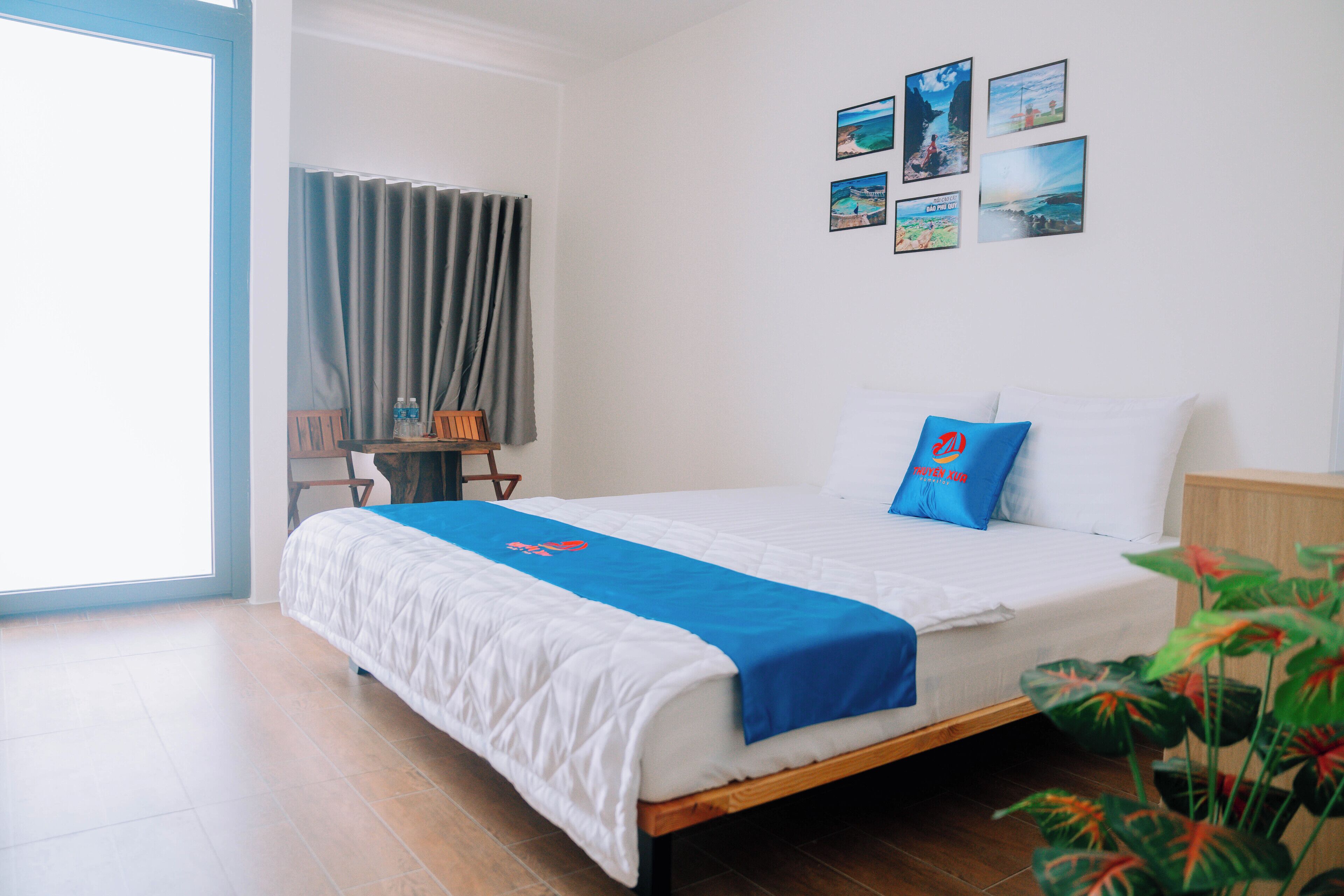 A hotel room with a bed, a desk, and a chair. There are pictures on the wall and a window with curtains.