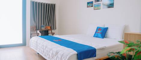 A hotel room with a bed, a desk, and a chair. There are pictures on the wall and a window with curtains.