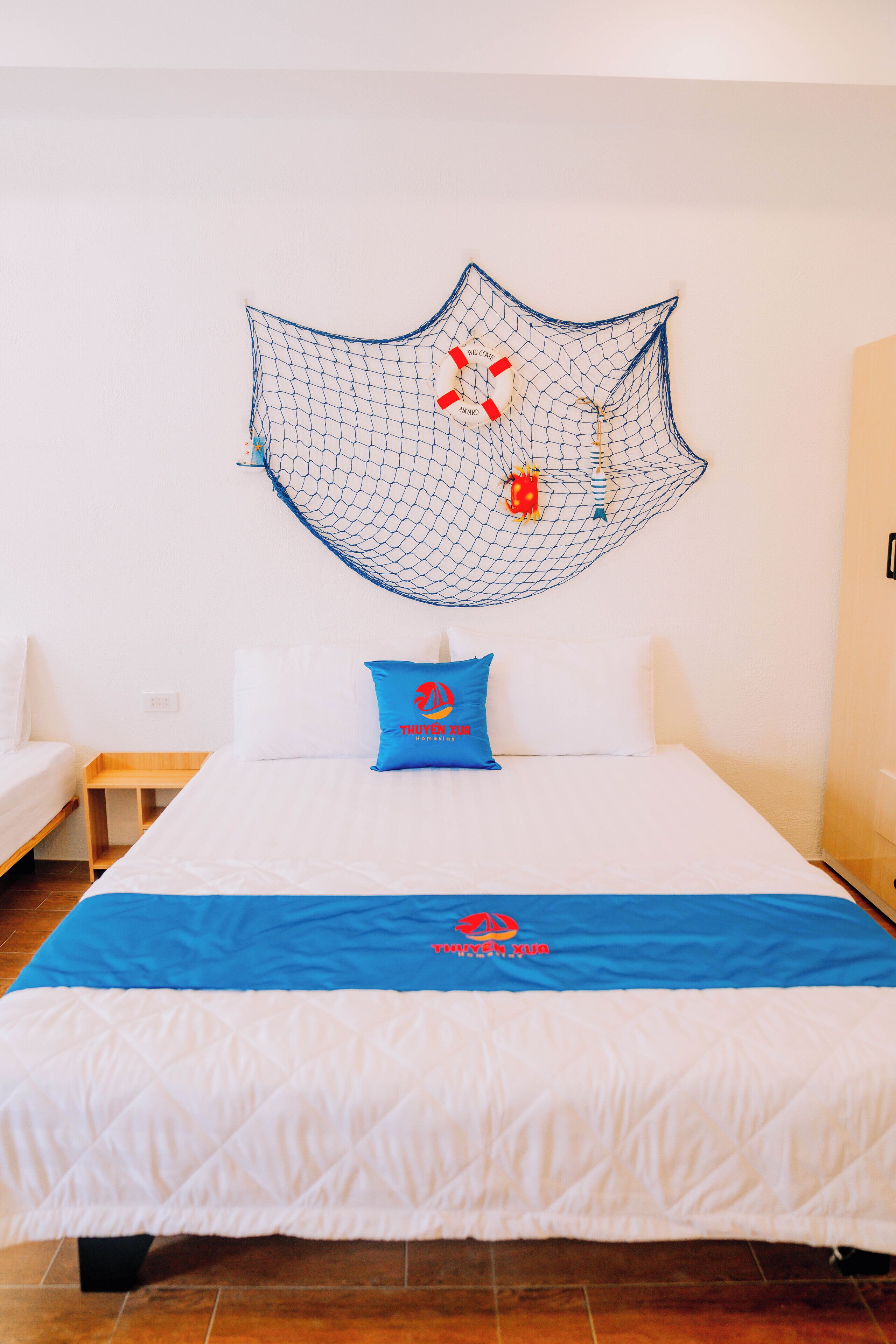 Ein Hotelzimmer mit einem Bett, einer blau-weißen Tagesdecke, einem blauen Kopfkissen und einer Netzdekoration an der Wand.