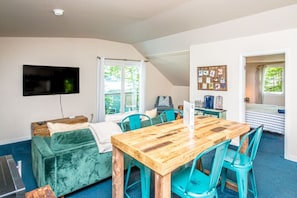 A cozy living room with a wooden dining table, teal chairs, a green sofa, and a flat-screen TV mounted on the wall. - Sunapee Sunset Cottage | Grill | Fire Pit (Newbury)