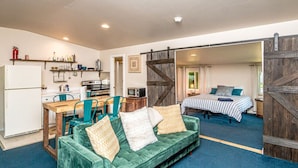 A compact living space with a kitchenette, a green sofa, a bed, and a large wooden door.