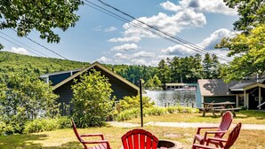 A lakeside cabin with a deck, outdoor seating, and a fire pit.