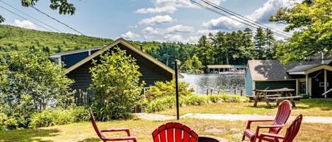 A lakeside cabin with a deck, outdoor seating, and a fire pit.