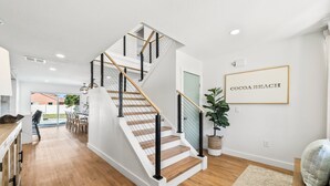 A staircase with wooden steps and black railings, leading to a room with a view of the outdoors. - Designer Home - 9 Beds - New Pool - By Beach (Cocoa Beach)