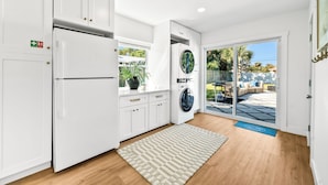 A modern kitchen with white cabinets, a built-in refrigerator, and a large window. - Designer Home - 9 Beds - New Pool - By Beach (Cocoa Beach)