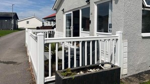 A single-story house with a white exterior, a porch with a white railing, and a small garden area with plants and a planter. - SeasideEscape-2Br-Sleeps4-Parking-PetsOK-Fireplace (Bridlington)