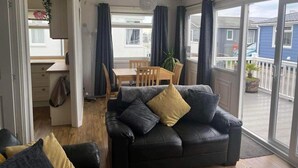 A cozy living room with a black leather sofa, a dining table with chairs, and a large sliding glass door leading to a balcony. - SeasideEscape-2Br-Sleeps4-Parking-PetsOK-Fireplace (Bridlington)