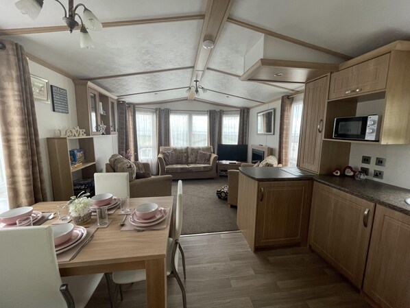 A spacious living area with a sofa, a dining table set for four, and a kitchen area with a microwave.