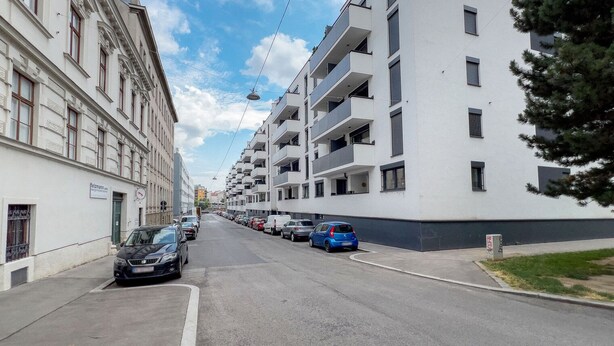 Una calle con edificios de apartamentos modernos, coches aparcados y cielo despejado.