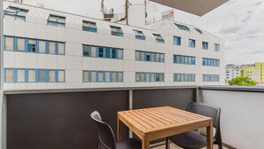 Un balcón con una mesa de madera y dos sillas, con vista a un edificio moderno con un letrero que dice "WIENER STADTISCHE".