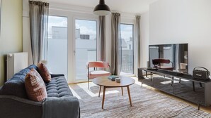 Un salon moderne avec un canapé, une table basse, un téléviseur et une petite table sur laquelle sont posés des livres.