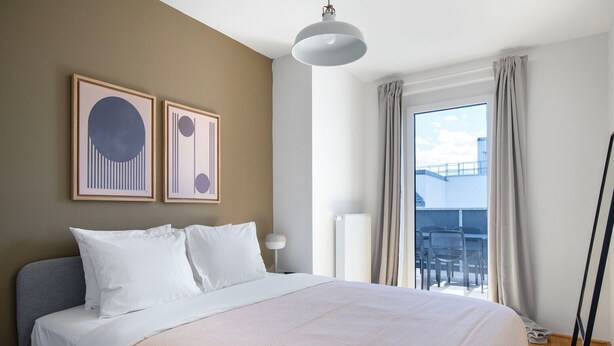 Une chambre d’hôtel avec un grand lit, une vue sur le ciel par la fenêtre et deux œuvres d’art encadrées au mur.