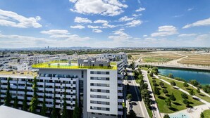 A modern building complex with multiple high-rise structures, a sports field, and a river in the background.