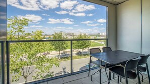 A balcony with a table and chairs, overlooking a cityscape with buildings and trees.