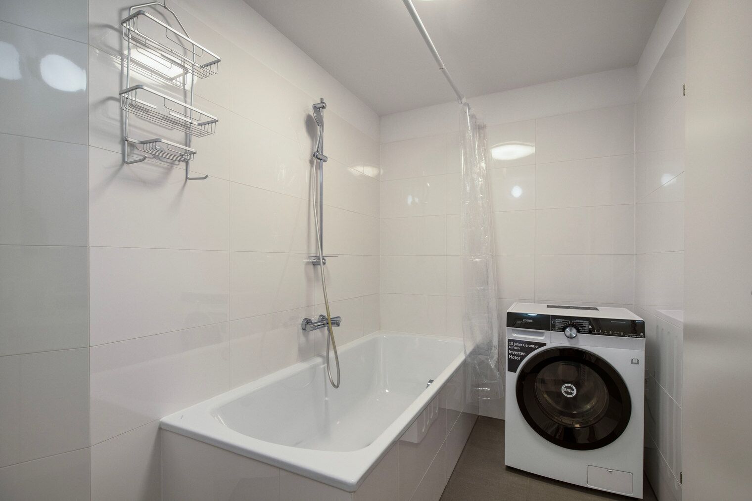Ein modernes Badezimmer mit einer weißen Badewanne, einer Dusche und einer integrierten Waschmaschine.