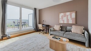 En moderne stue med en grå sofa, et træbord og et stort vindue med gardiner.