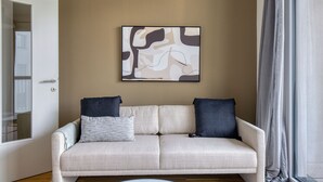 Ein Wohnzimmer mit einem beigefarbenen Sofa, zwei dunklen Kissen und einem modernen abstrakten Gemälde an der Wand.