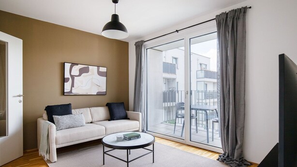 Ein modernes Wohnzimmer mit einer Couch, einem Couchtisch und einem großen Fenster mit Vorhängen.