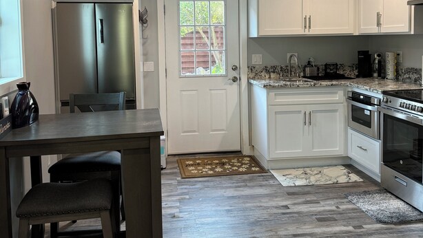 A modern kitchen with white cabinets, stainless steel appliances, and a wooden dining table. - The Tiny cottage in quite charming. Palos Verdes with AC, WiFi and washer/dryer  (Rancho Palos Verdes)