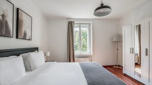 A modern hotel room with a large bed, a bedside table, a floor lamp, and a wardrobe.
