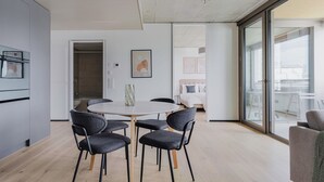 Un espace de vie moderne à aire ouverte, comprenant une table de salle à manger ronde, six chaises et une grande porte-fenêtre coulissante donnant sur un balcon.