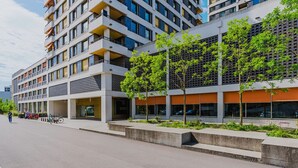 Un immeuble moderne à plusieurs étages, doté de balcons, de grandes fenêtres et d’un espace paysager agrémenté d’arbres.