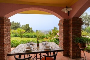 Ein Essbereich im Freien mit einem Tisch für zwei Personen, einer Champagnerflasche und Blick aufs Meer.