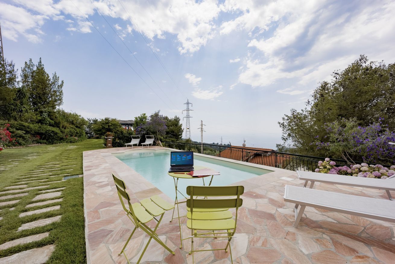 A poolside area with a laptop on a table, two chairs, and a bench.