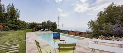A poolside area with a laptop on a table, two chairs, and a bench.