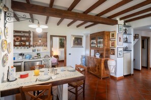Una cucina rustica con travi in legno, un tavolo da pranzo apparecchiato con piatti e una brocca, e diversi utensili da cucina.