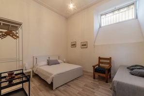 Un dormitorio con cama, una silla, una mesita de noche, un armario y una ventana.
