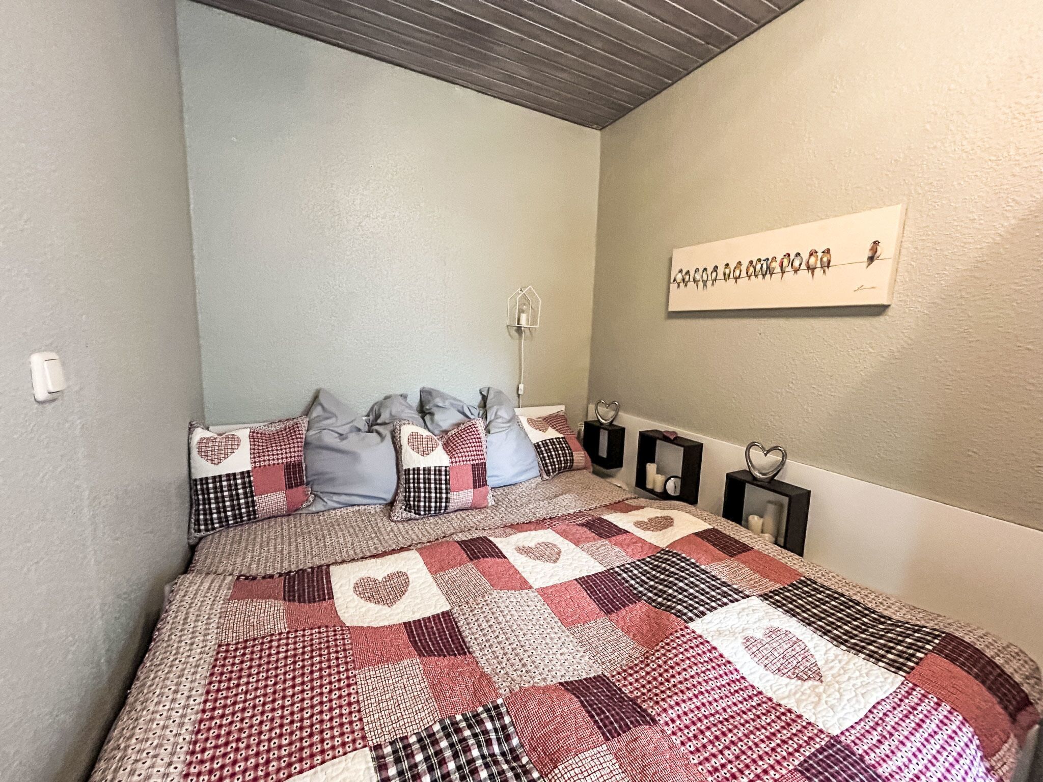 Ein Schlafzimmer mit einem Patchwork-Quilt, einer Vogelkunst an der Wand und herzförmigen Dekorationen.