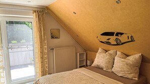 Ein Schlafzimmer mit Bett, Heizkörper, einem Fenster mit Vorhängen und einer Wandsticker mit einem Auto-Motiv.