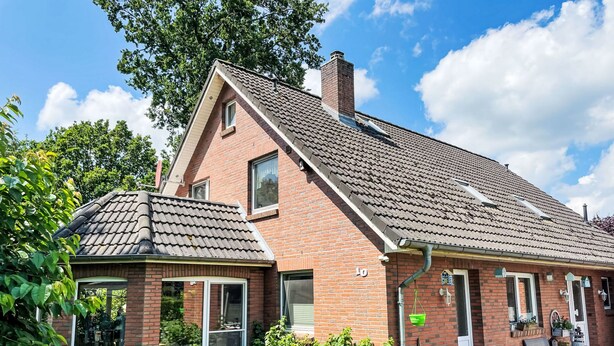 Ein zweigeschossiges Backsteinhäuschen mit geneigtem Dach, großen Fenstern und einer kleinen angebauten Garage.