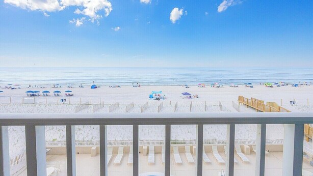 Une vue sur la plage depuis un balcon équipé de chaises longues et de parasols.