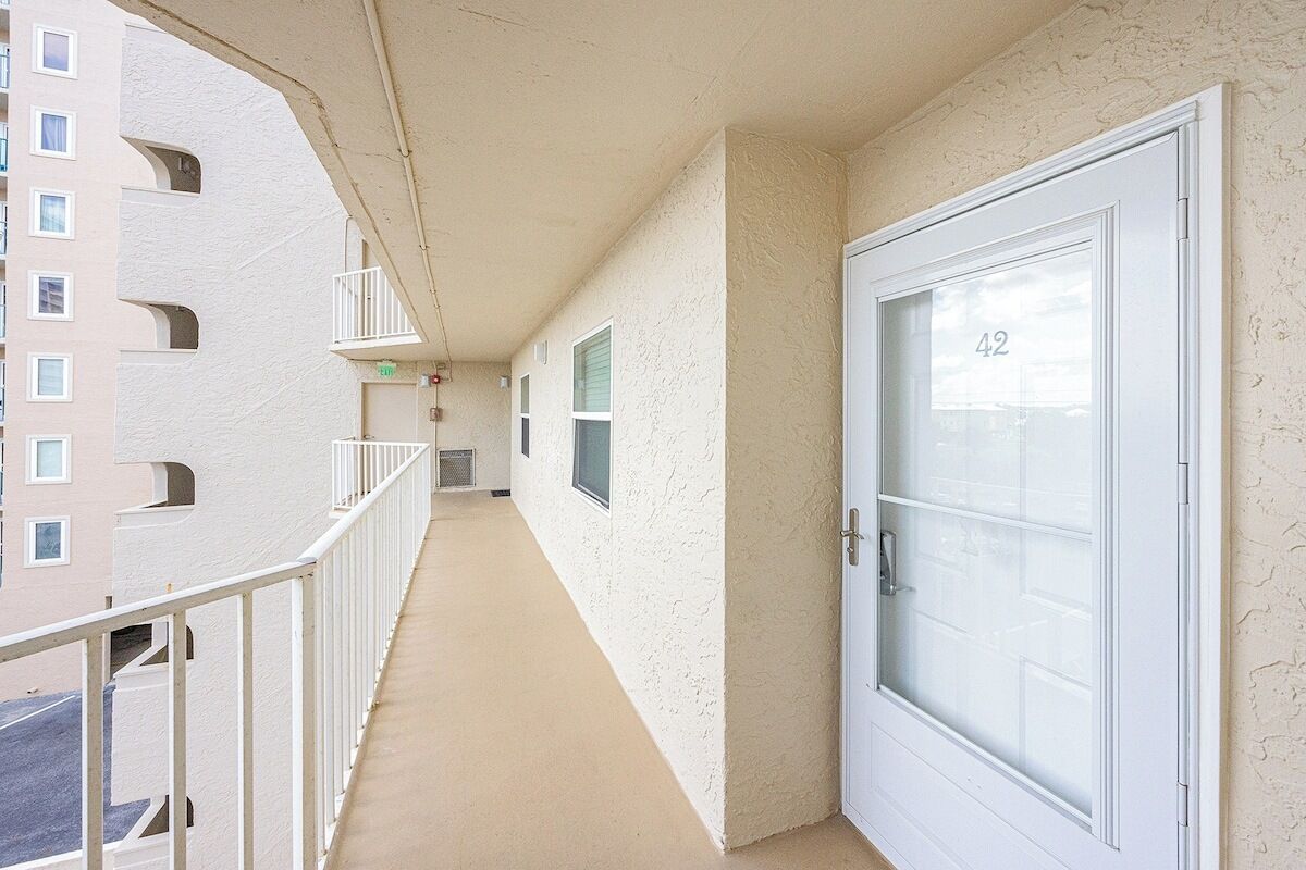 A corridor with a white door marked "42", a balcony with white railings, and a building with multiple windows.