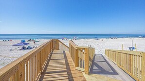 Une promenade en bois menant à une plage où l’on trouve des parasols et des chaises de plage.