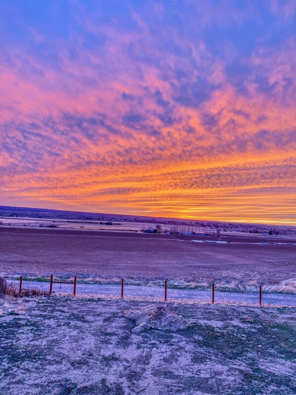 A rural landscape with a fence in the foreground and a sunset in the background.
