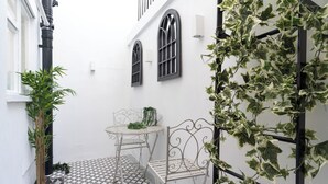 A small outdoor patio with a tiled floor, two metal chairs, a small table, and potted plants. - Central Apartment with Patio - Sofa Bed (Cheltenham)