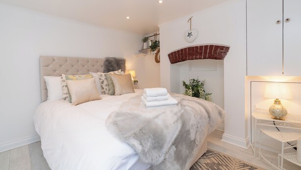 A modern bedroom with a tufted headboard, a fireplace, a bedside table with a lamp, and a neatly made bed. - Central Apartment with Patio - Sofa Bed (Cheltenham)