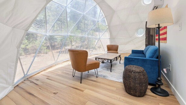 A tent-like room with a wooden floor, a table, two chairs, a sofa, and a lamp.