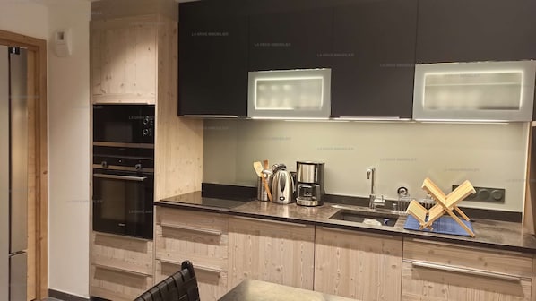 A modern kitchen with wooden cabinets, stainless steel appliances, and a built-in oven. - Paradiski new, quiet and sunny Plan peisey (PEISEY-NANCROIX)